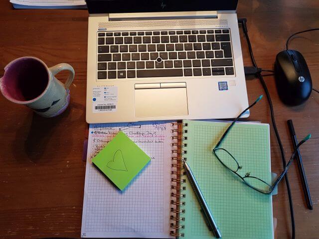 Ein aufgeräumter Schreibtisch mit Laptop, Notizbuch, Brille und Kaffeetasse
